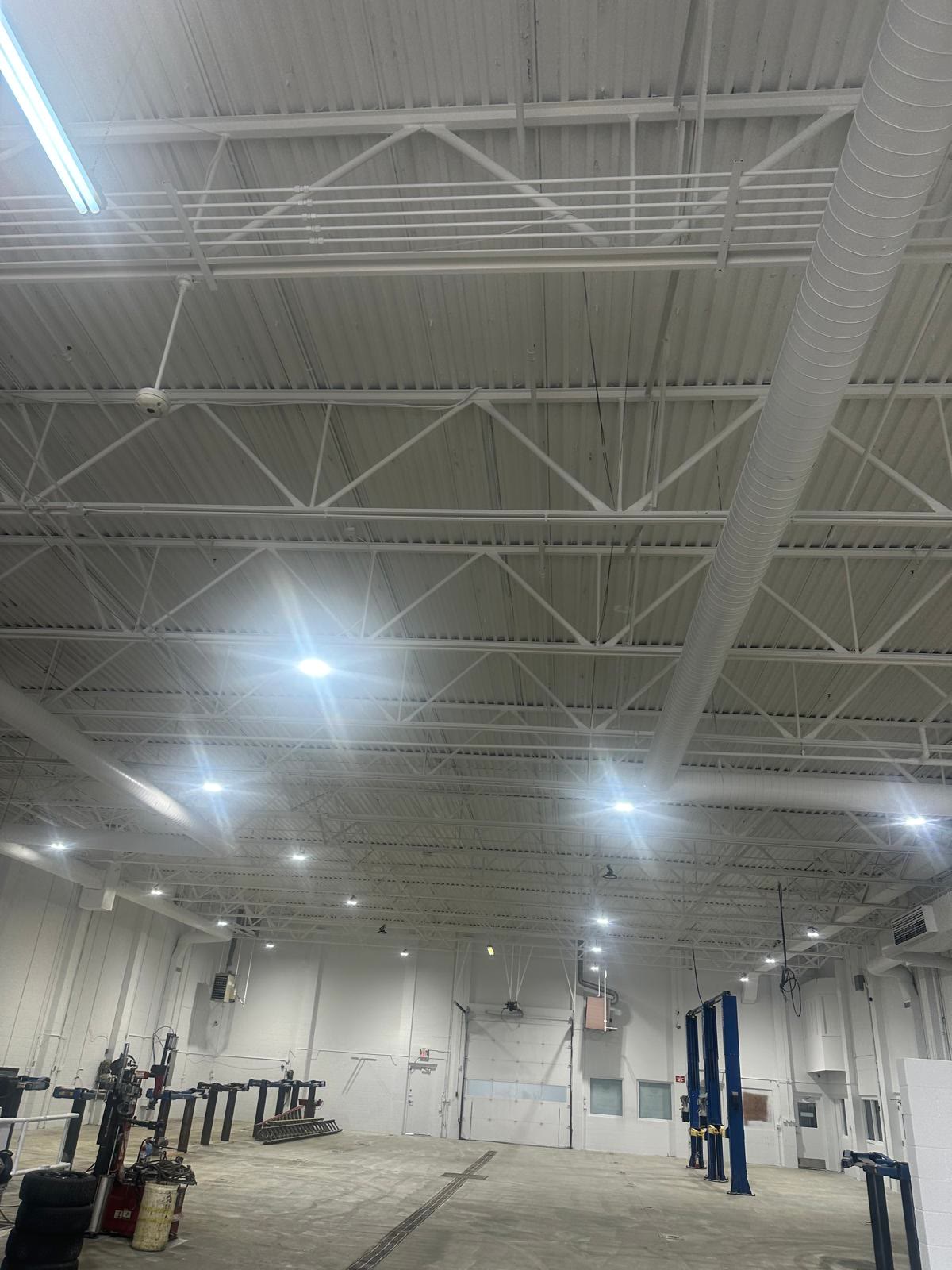 The same shop ceiling after painting: steel deck and open trusses sprayed a uniform white