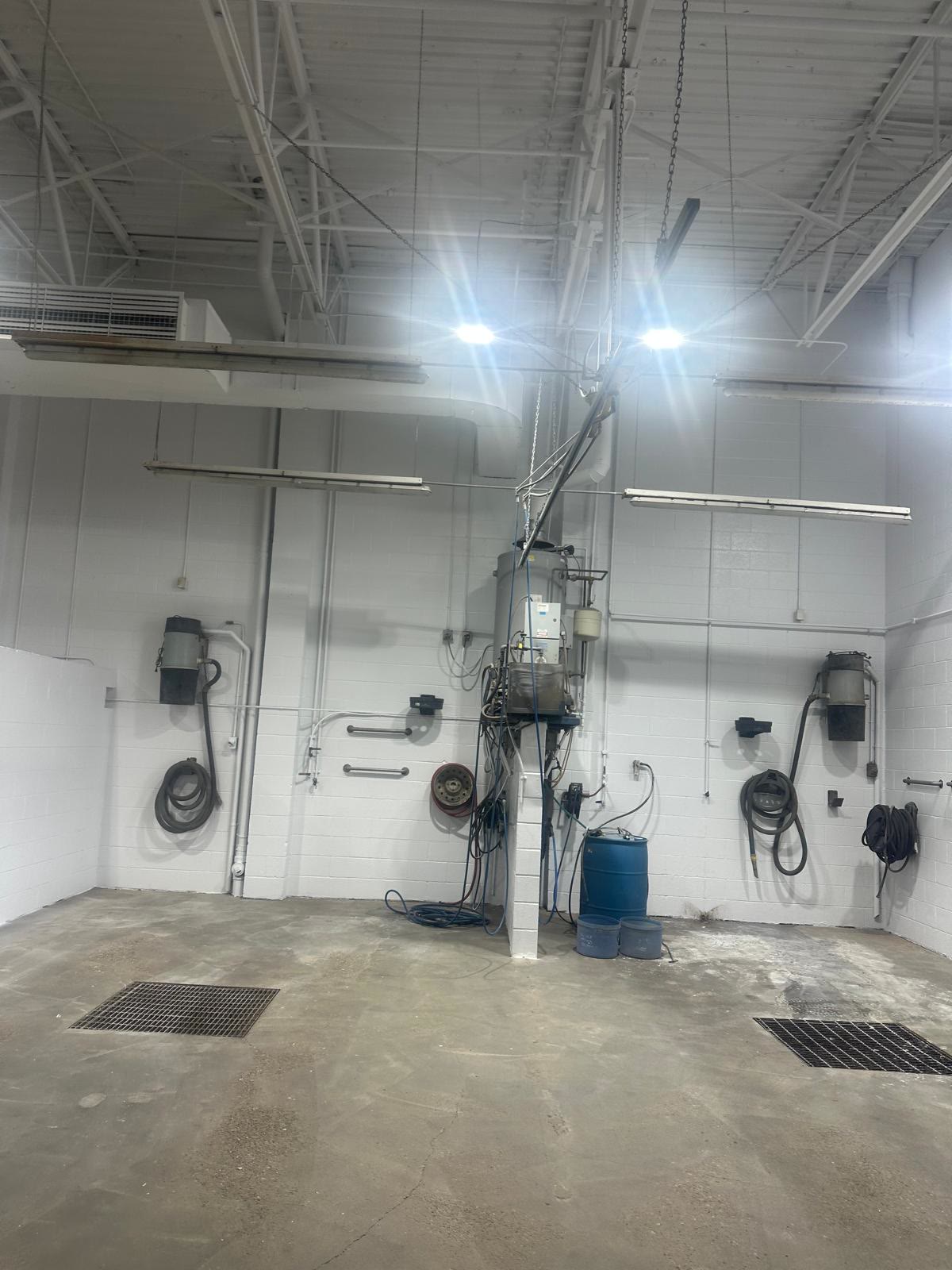 The same wash bay corner after painting: clean bright white block walls with the hose reels and equipment reinstalled
