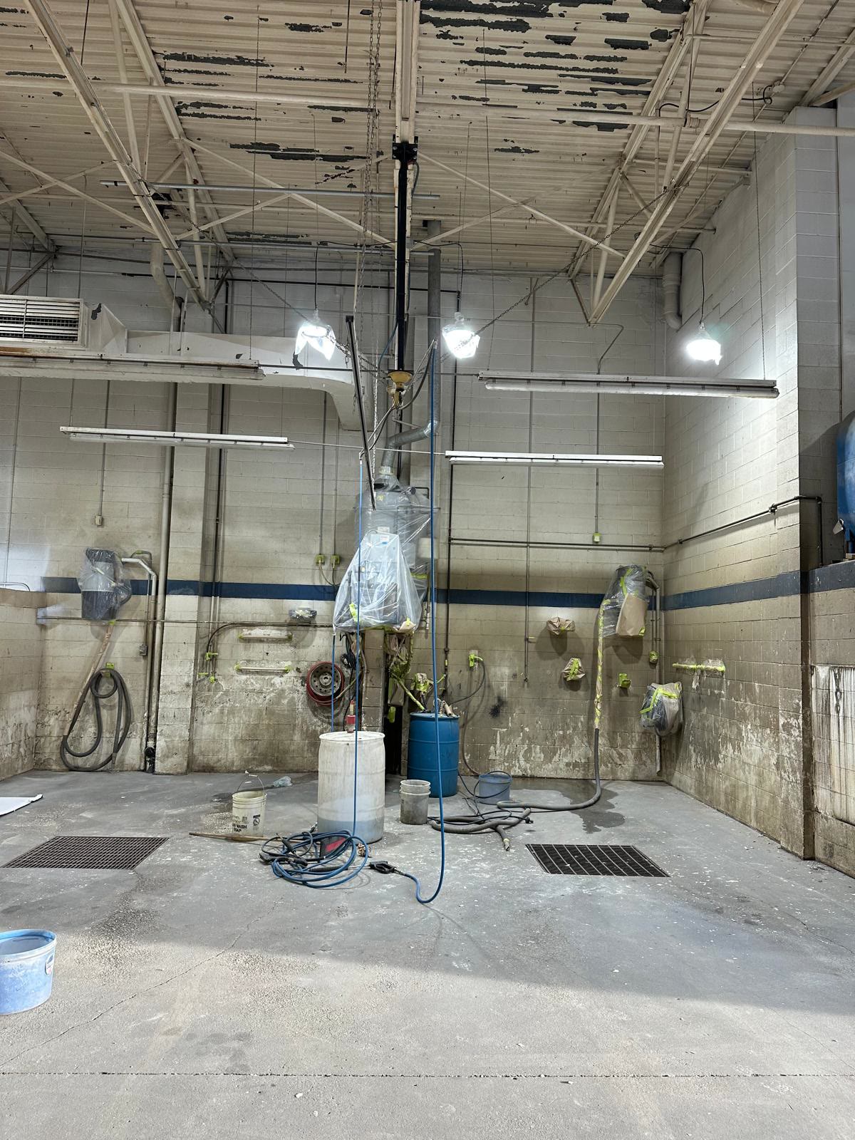 Wash bay corner before painting: grimy concrete block walls with a faded blue stripe and water staining