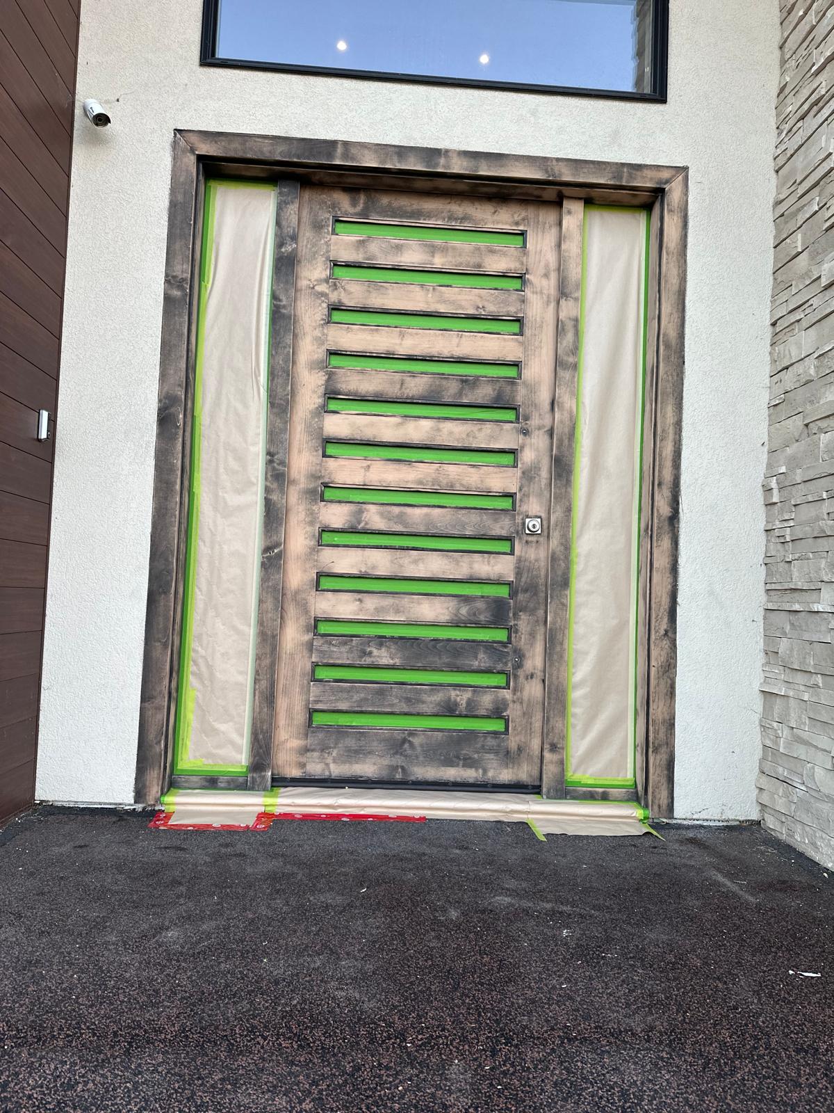 A front entrance door in raw, unfinished wood masked with green tape before Bright Star refinished it