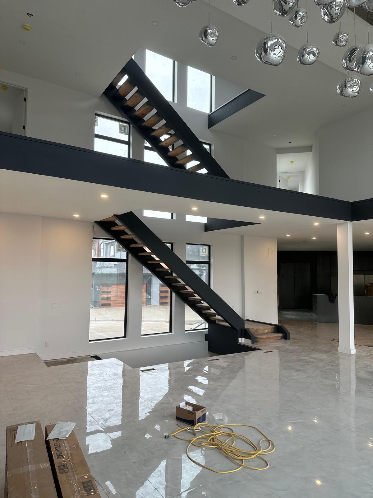 The finished great room with a black floating staircase, polished marble floor, and orb chandelier
